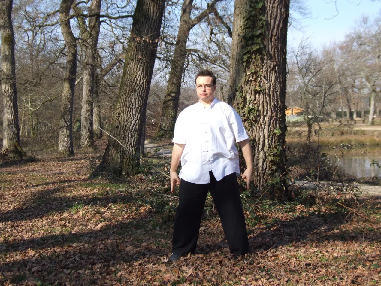Michel Brunet en tenue traditionnelle chinoise, posture de pratique en extérieur, France